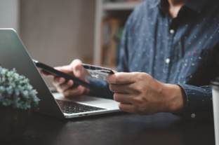 Mann mit Handy in der Hand sitzt vor einem Laptop