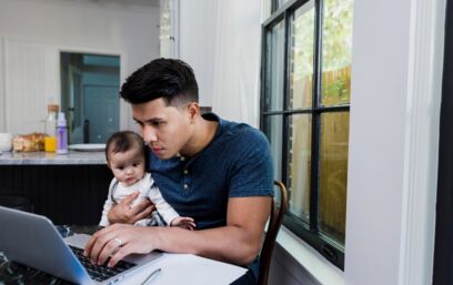 Mann arbeitet am Laptop mit Baby auf dem Schoss