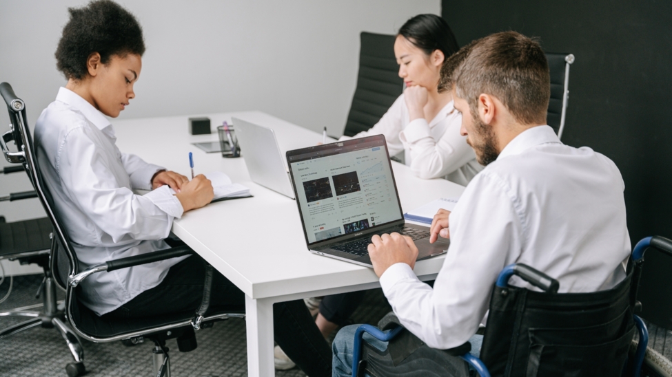 Drei Personen sitzen an einem Tisch und Arbeiten