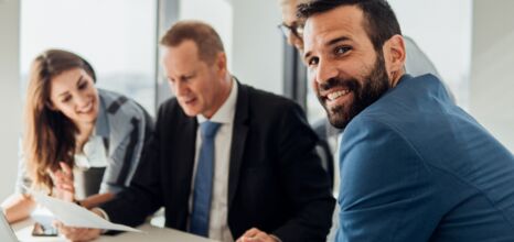 Vier Personen sitzen an einem Tisch und ein Mann schaut in die Kamera